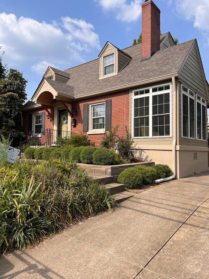 Brick house with a small porch and manicured front yard under a blue sky.