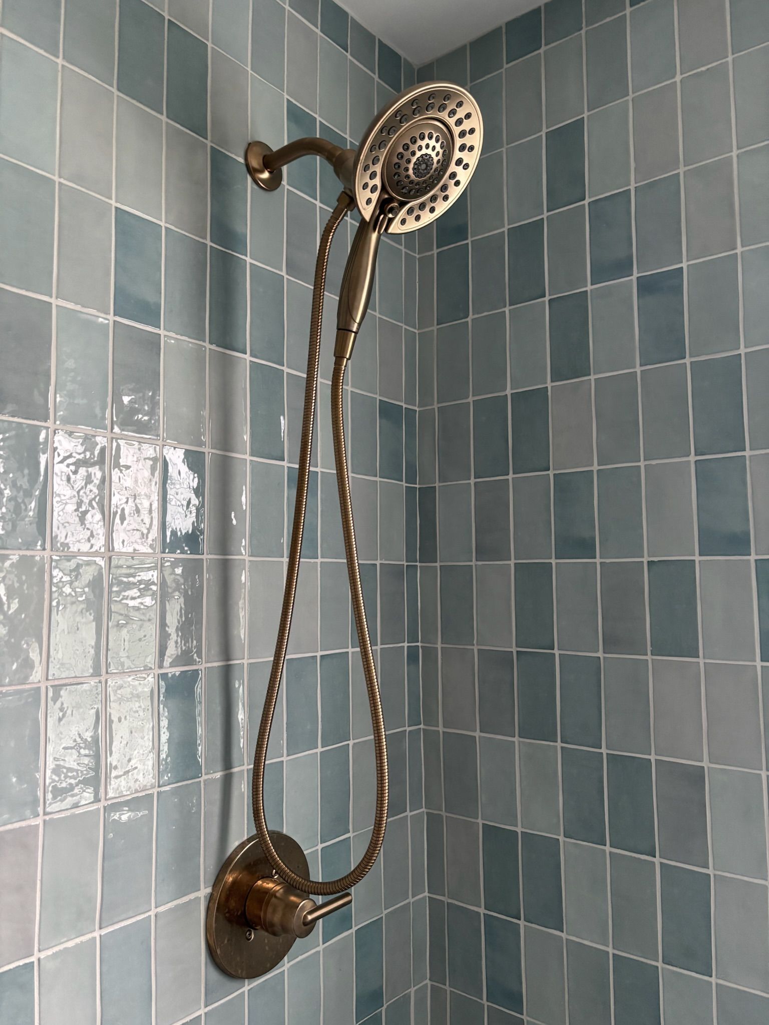 Bronze shower head and hose on blue tiled wall.