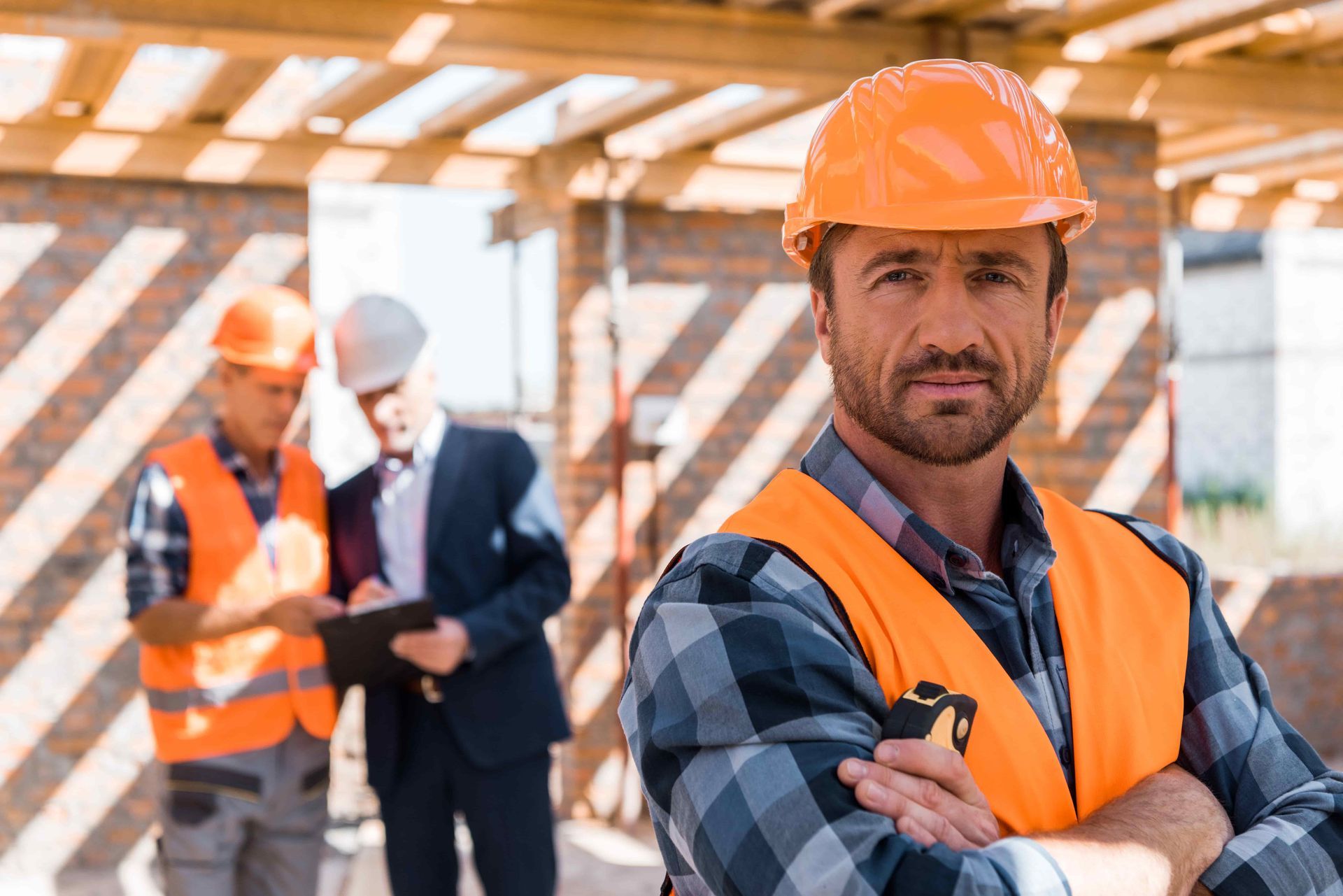 A construction worker is standing with his arms crossed on a construction site.