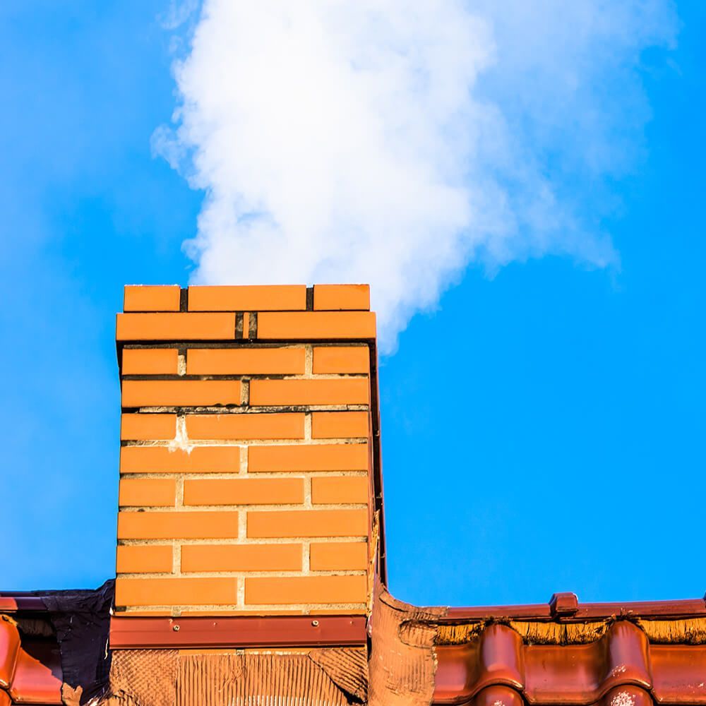 A brick chimney with smoke coming out of it against a blue sky.
