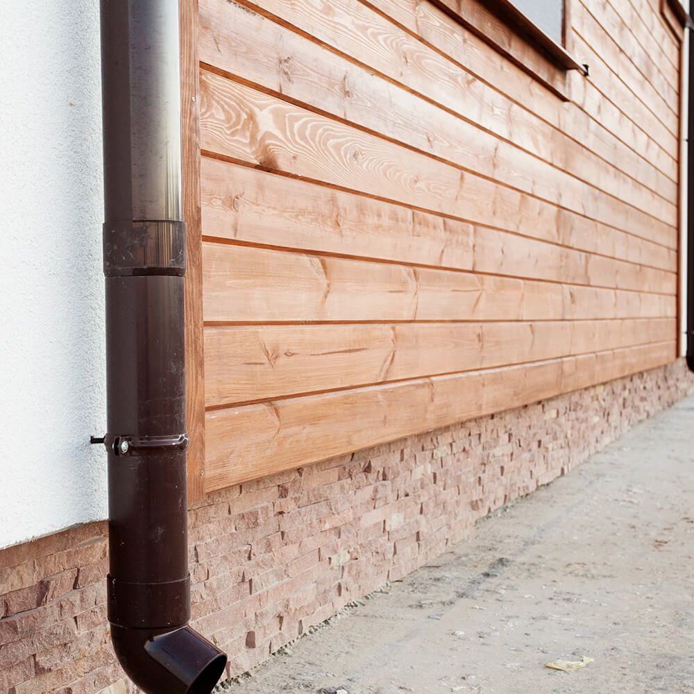 A brown drainpipe is attached to the side of a wooden building.
