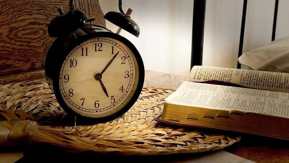 An alarm clock is sitting on a table next to a bible.