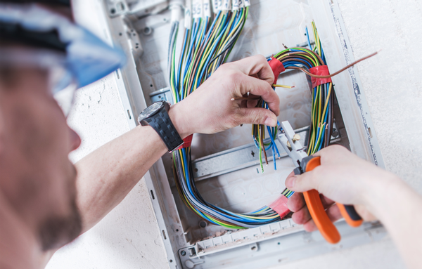 Electricista trabajando con cables dentro de un panel, utilizando alicates.