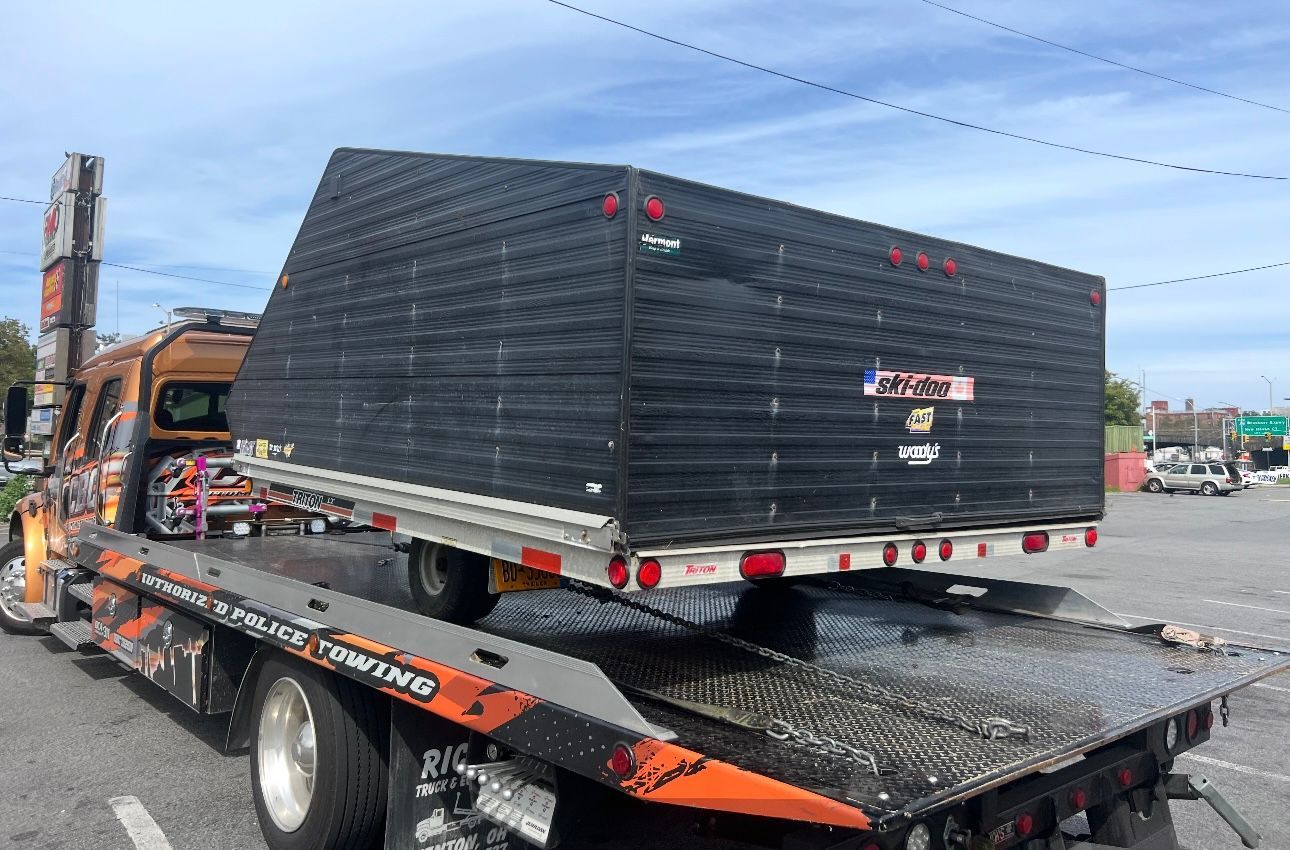 A tow truck is carrying a large black box on the back of it.