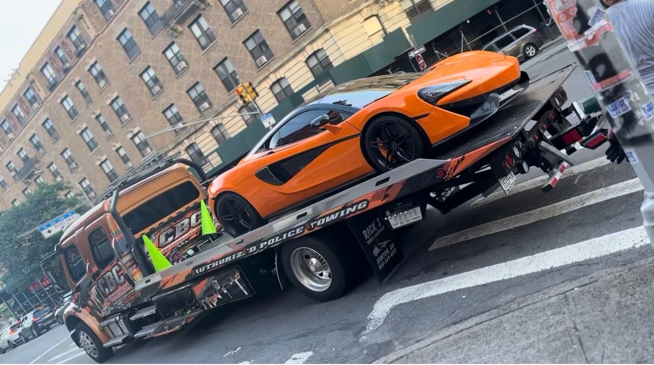 An orange sports car is being towed by a tow truck