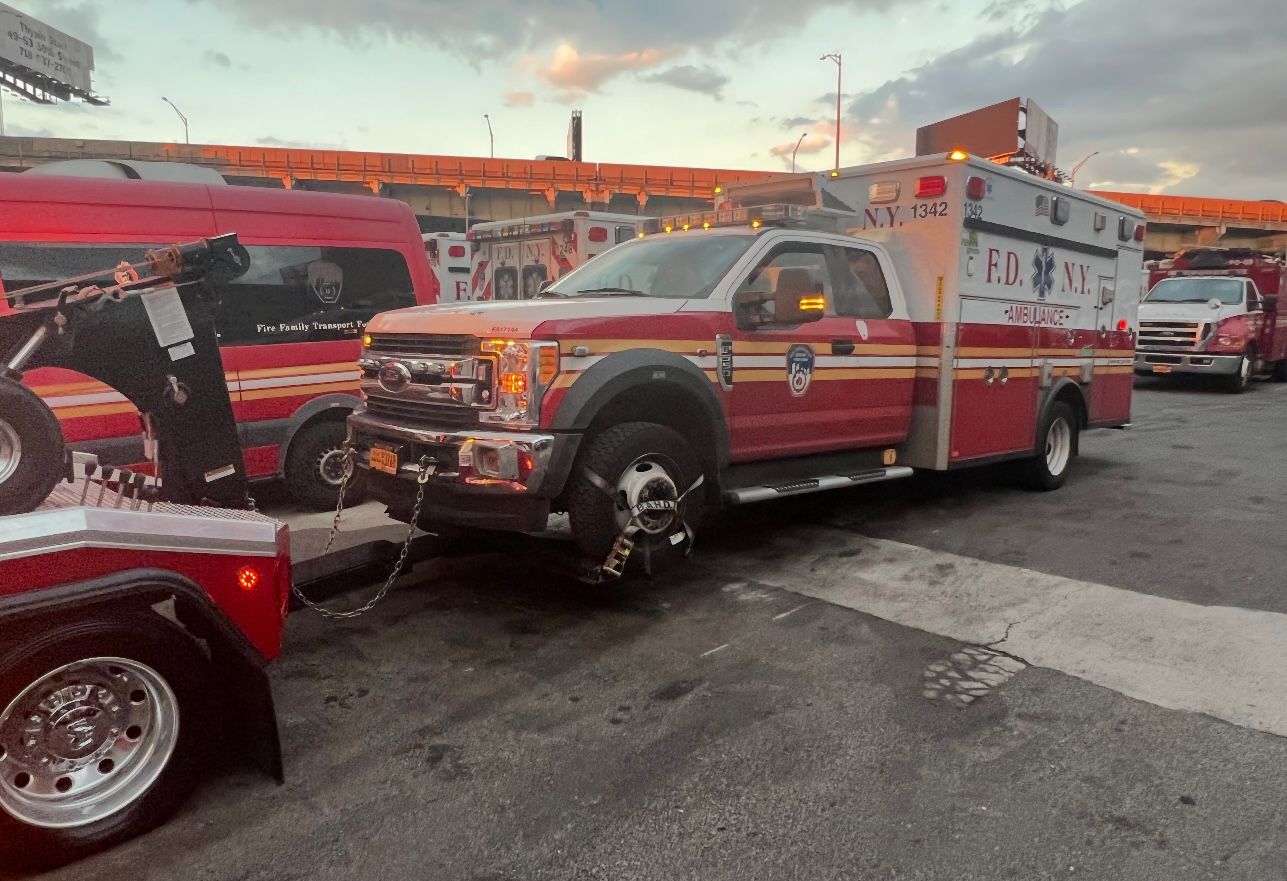 A red ambulance is being towed by a tow truck.