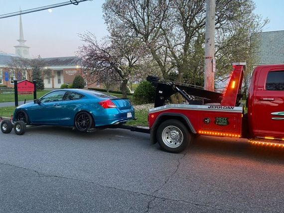 A blue car is being towed by a red tow truck.