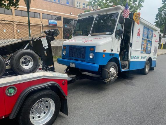 A blue and white ice cream truck is being towed by a tow truck.