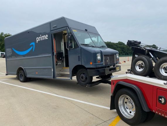 An amazon delivery truck is being towed by a tow truck.