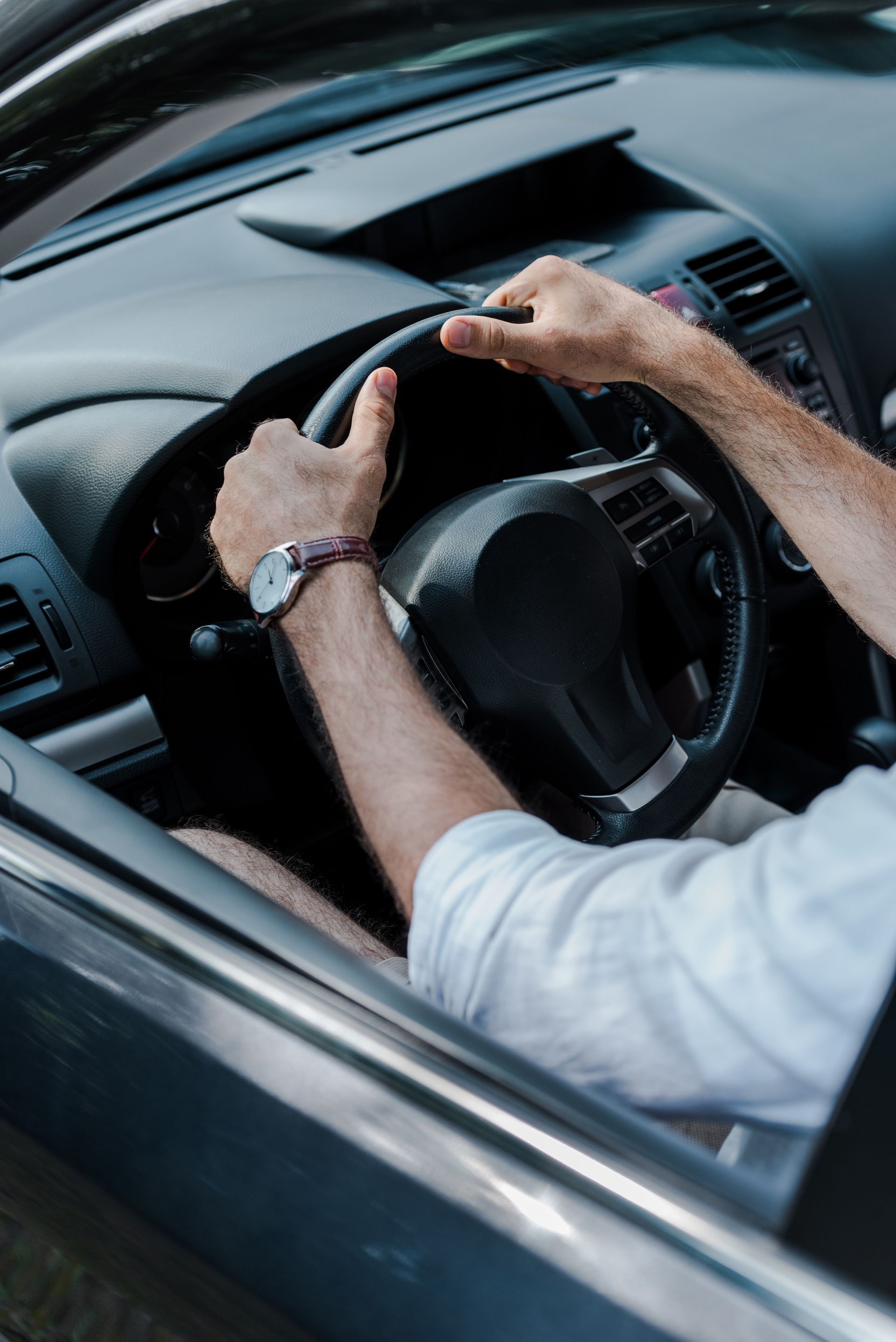 Person's hands gripping a steering wheel inside a car, wearing a watch.