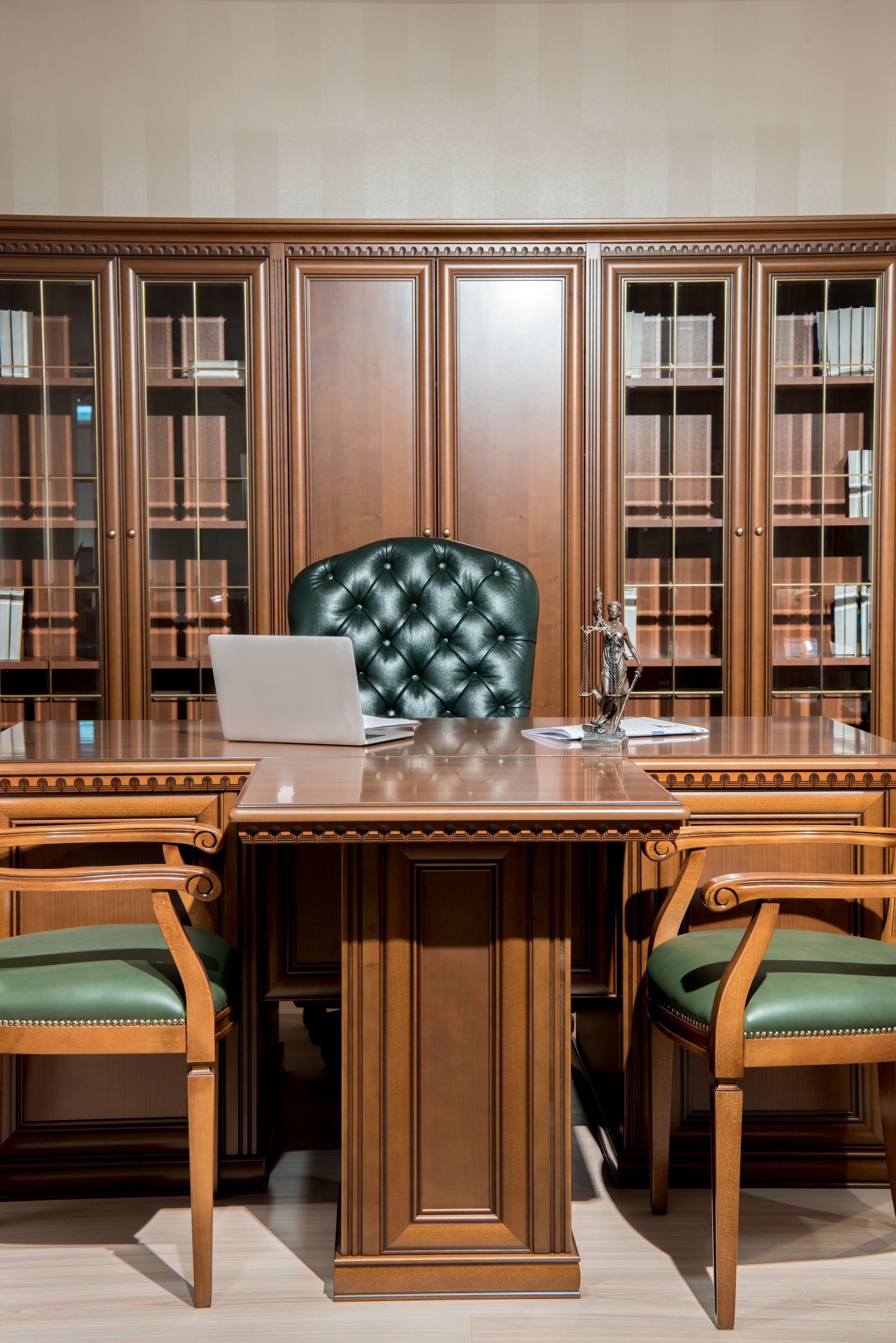Wooden office with desk, green chairs, and built-in bookcase, with laptop and statue.