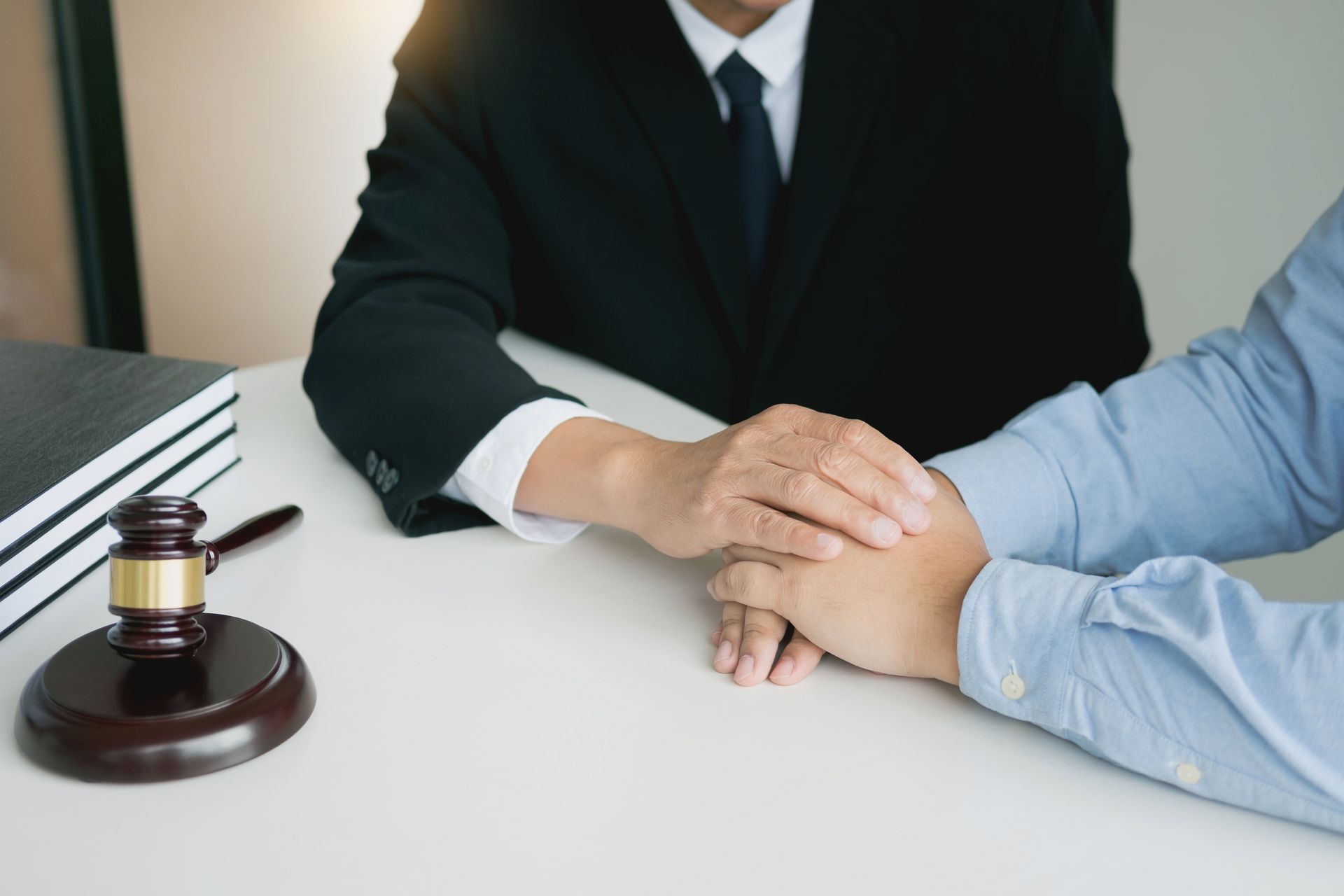 Lawyer comforts client; hands clasped, gavel, legal books on desk.