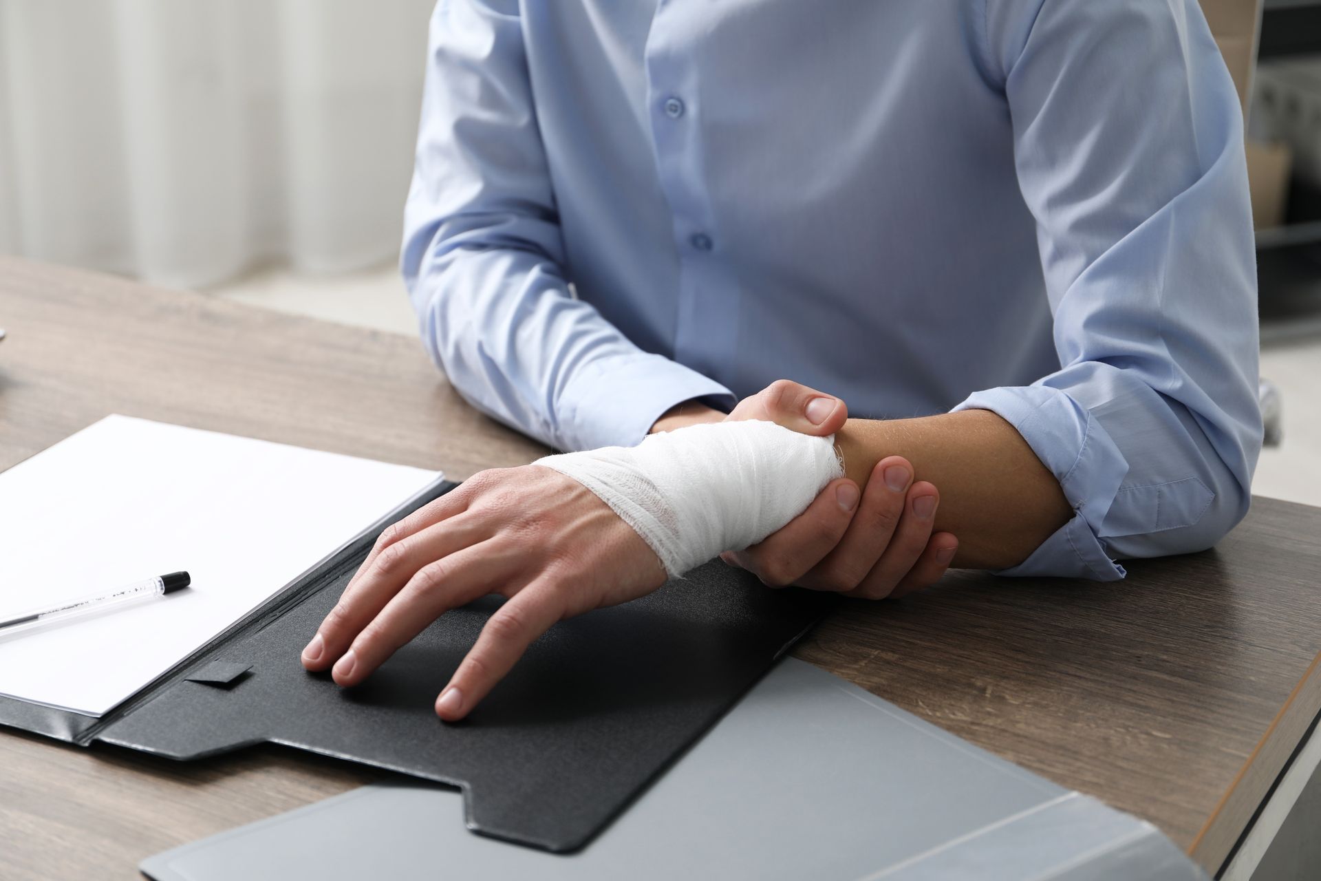 Man in blue shirt at desk, holding bandaged wrist.