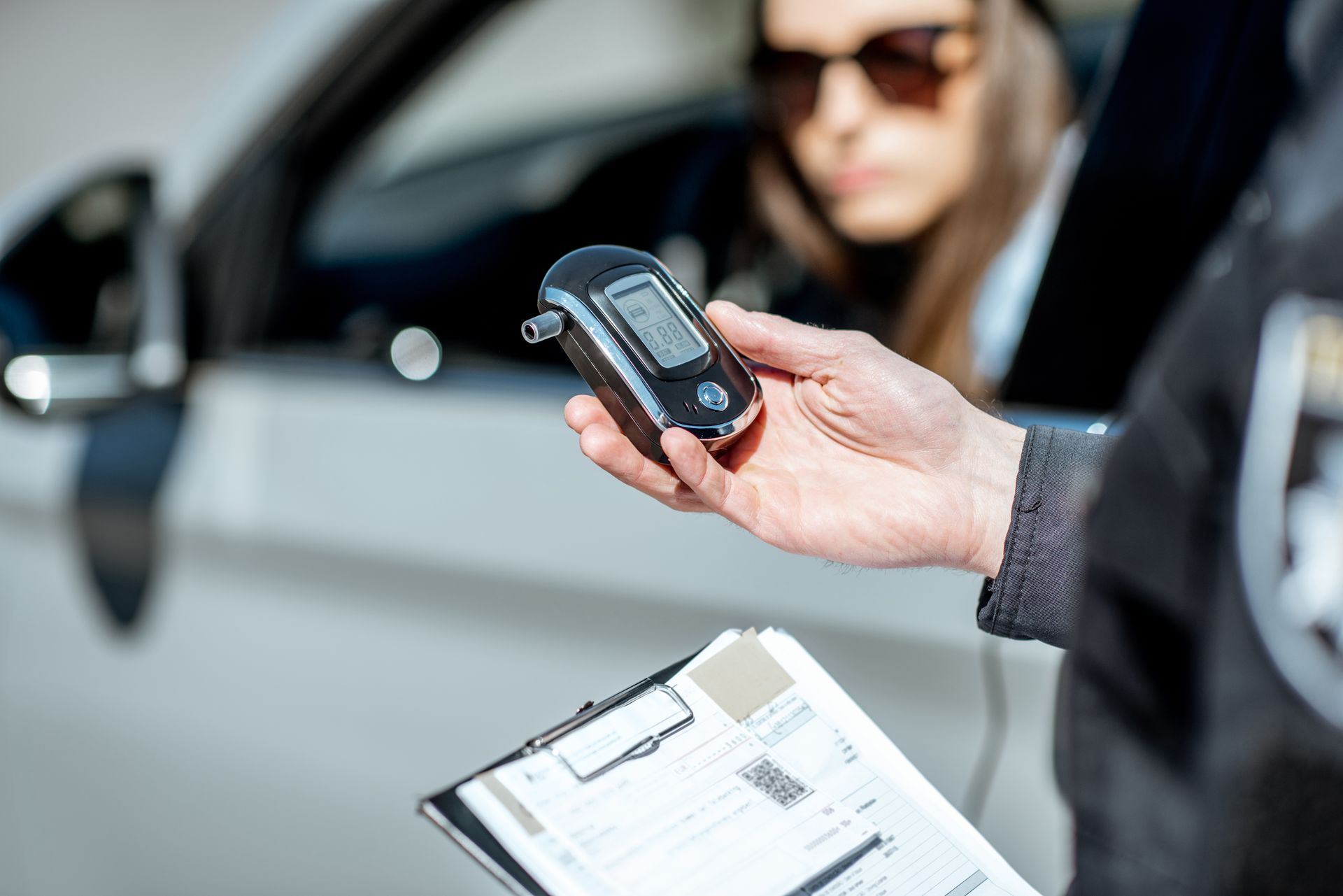 Police officer holding a breathalyzer near a driver in a car.
