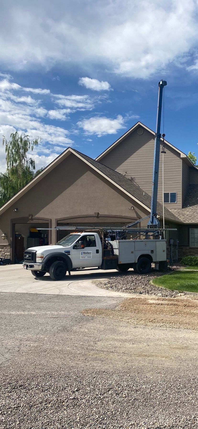White pickup and utility trailer parked beside a beige house under a cloudy sky.