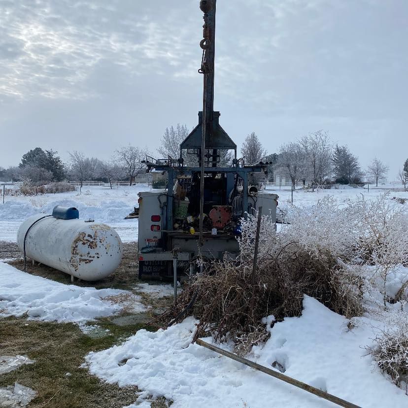 Snowy rural scene with a propane tank and drilling rig beside dried grass under an overcast sky