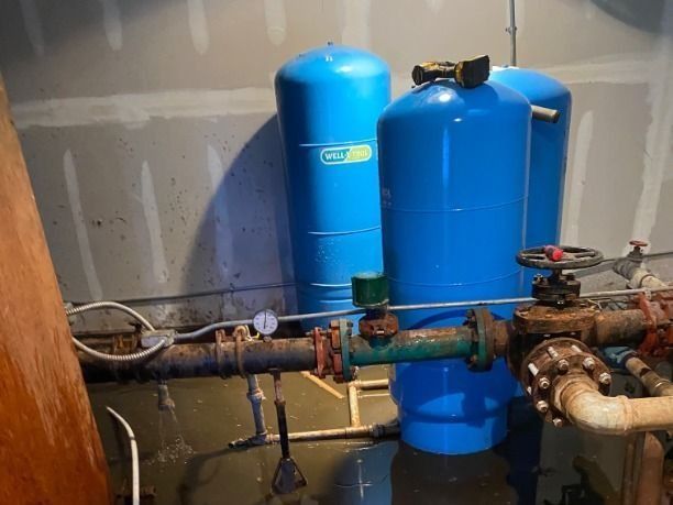 Blue water tanks and plumbing pipes in a utility room with unfinished walls.