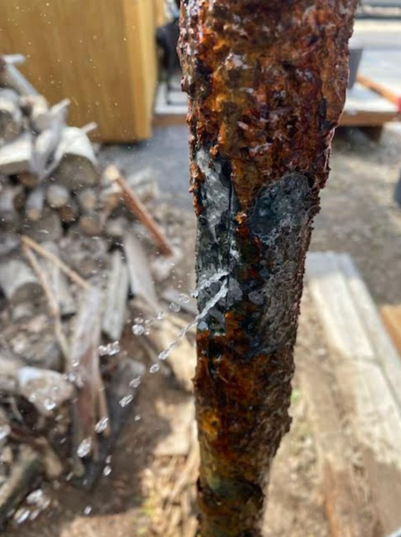 Close-up of a rusted, charred metal pole with peeling corrosion and blackened patches.