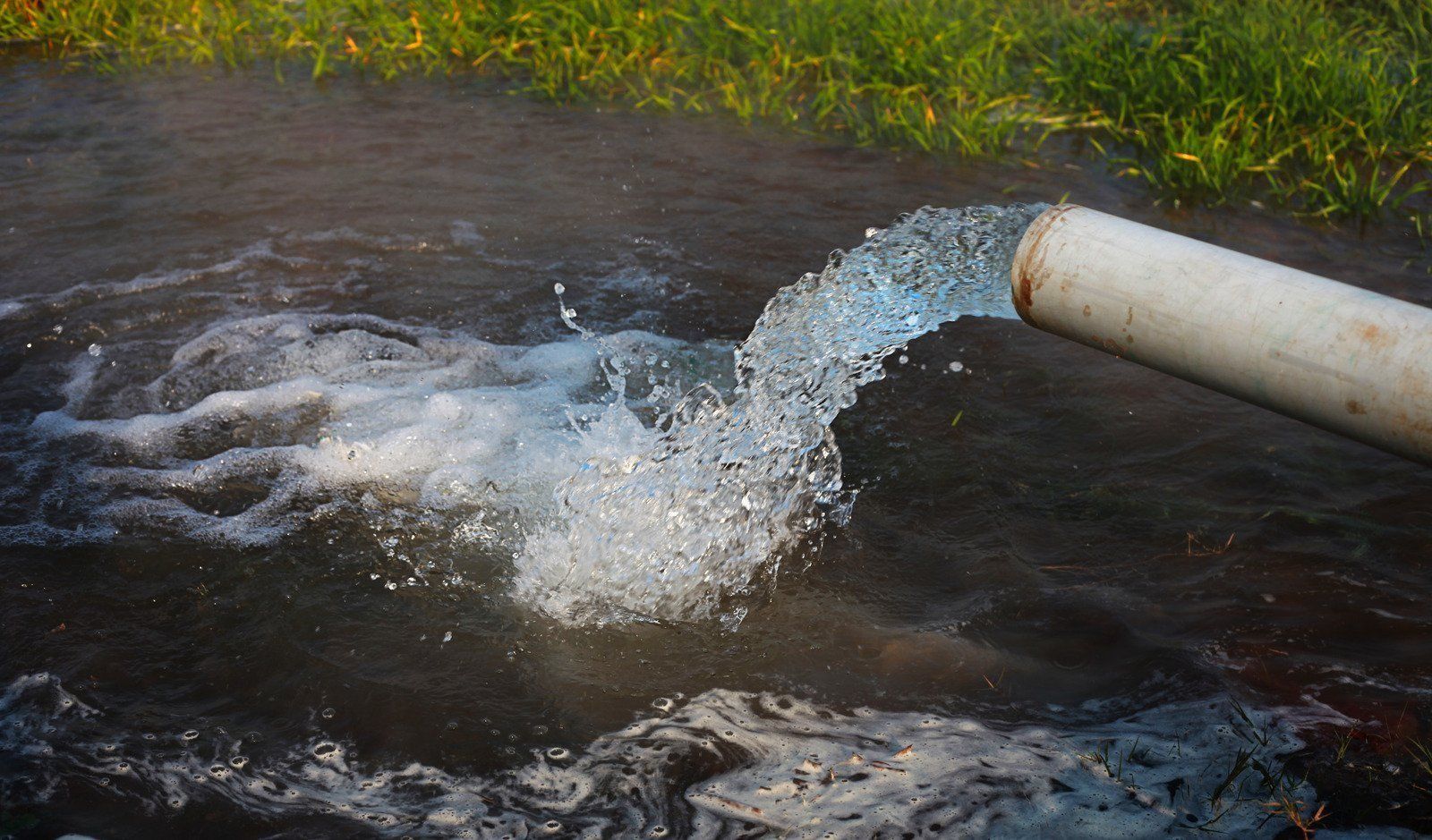 Water gushing from a white pipe into a dark stream, creating splashes and ripples.