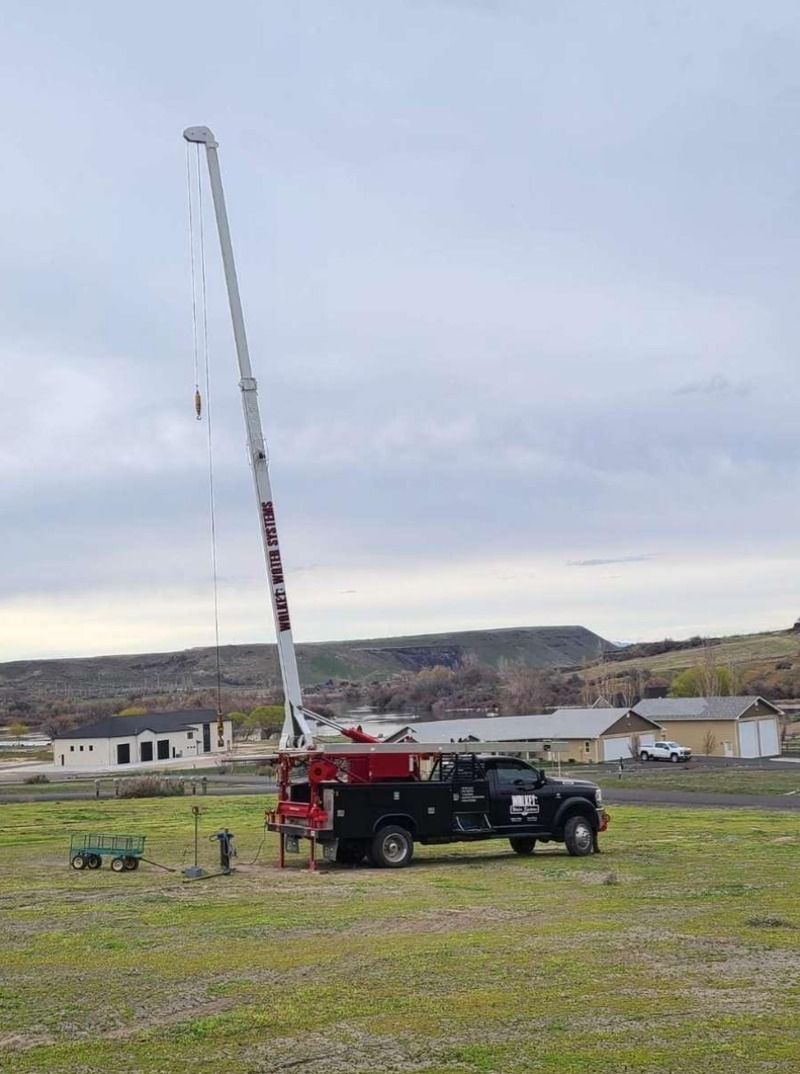 Red crane truck with extended boom parked in a grassy field under a cloudy sky