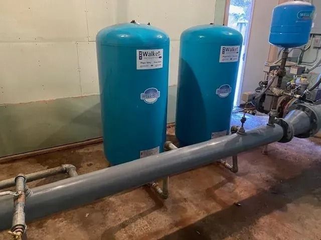 Industrial pump room with blue pressure tanks and large gray pipes along the floor