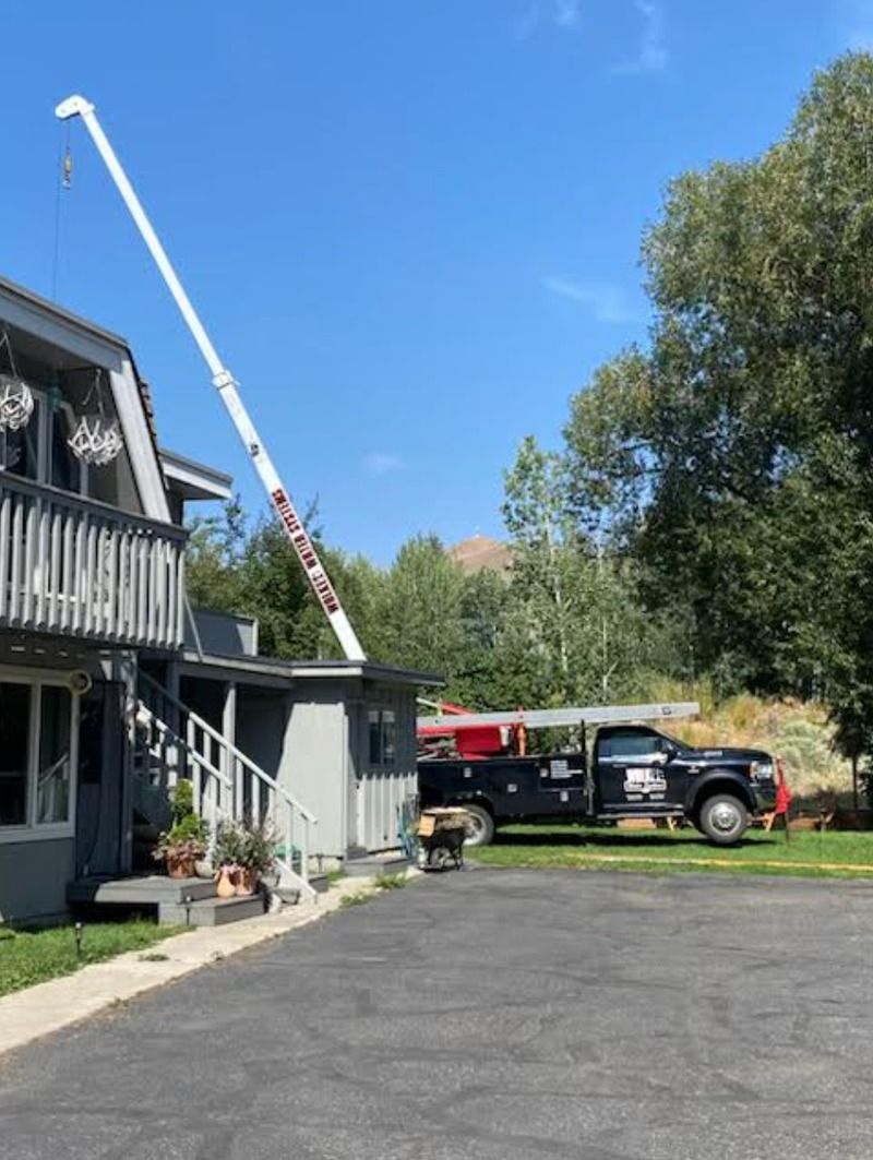 House with a raised ladder truck and a black pickup in a driveway under a clear blue sky