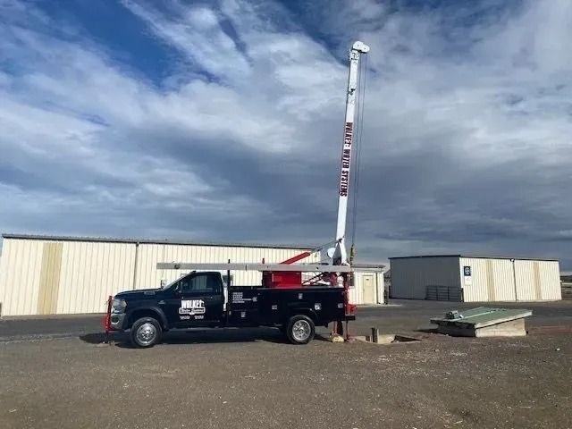 Black utility truck with raised boom parked by a beige building under a cloudy sky.