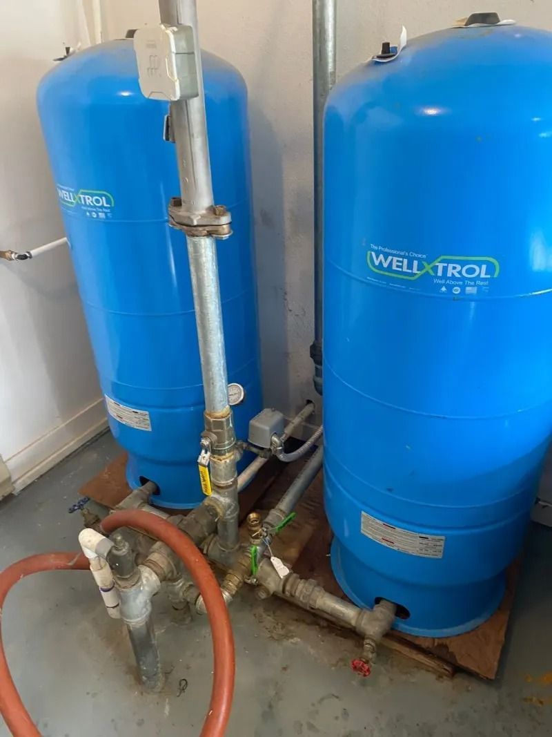 Two blue water filtration tanks with connected pipes in a utility room