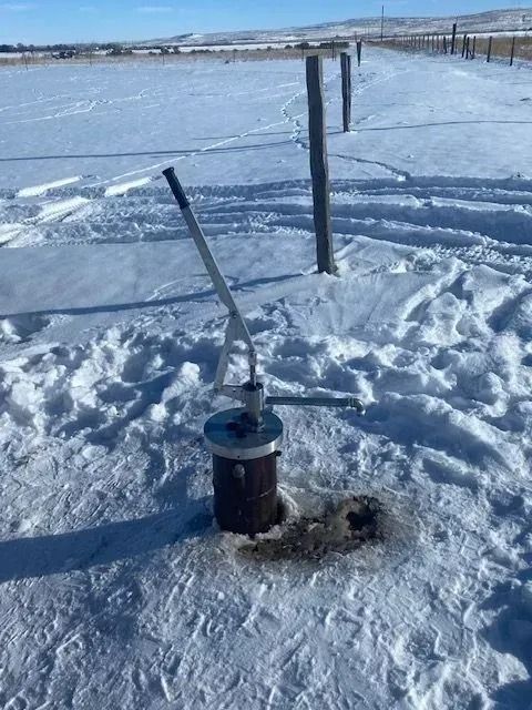 Snow-covered frozen field with poles and a small utility device in the foreground under a clear sky