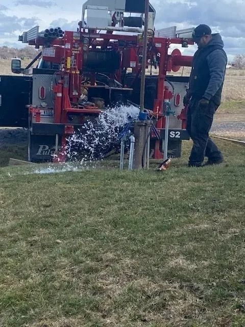 Worker operating red agricultural machine spraying water in a grassy field