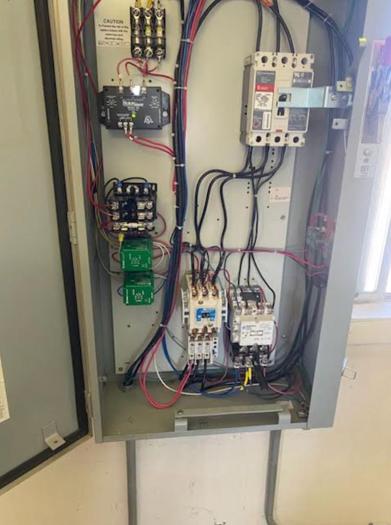 Open electrical control panel with wires, breakers, relays, and components mounted inside a metal cabinet.