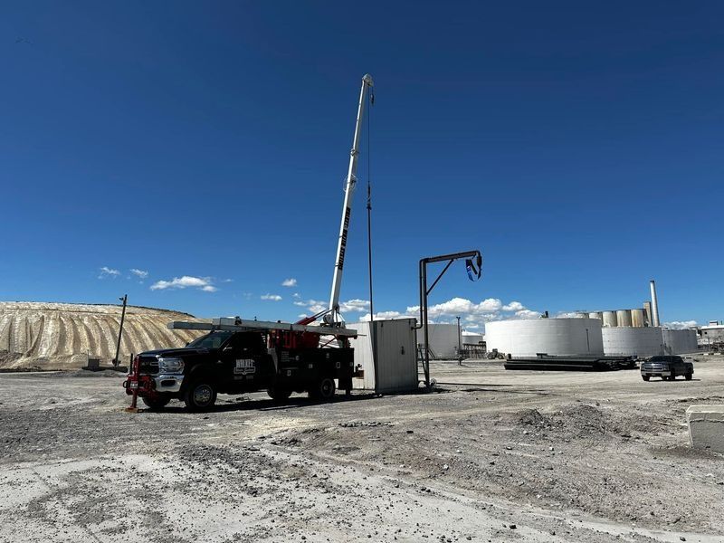 Oil field with truck-mounted drilling rig beside storage tanks under a clear blue sky.