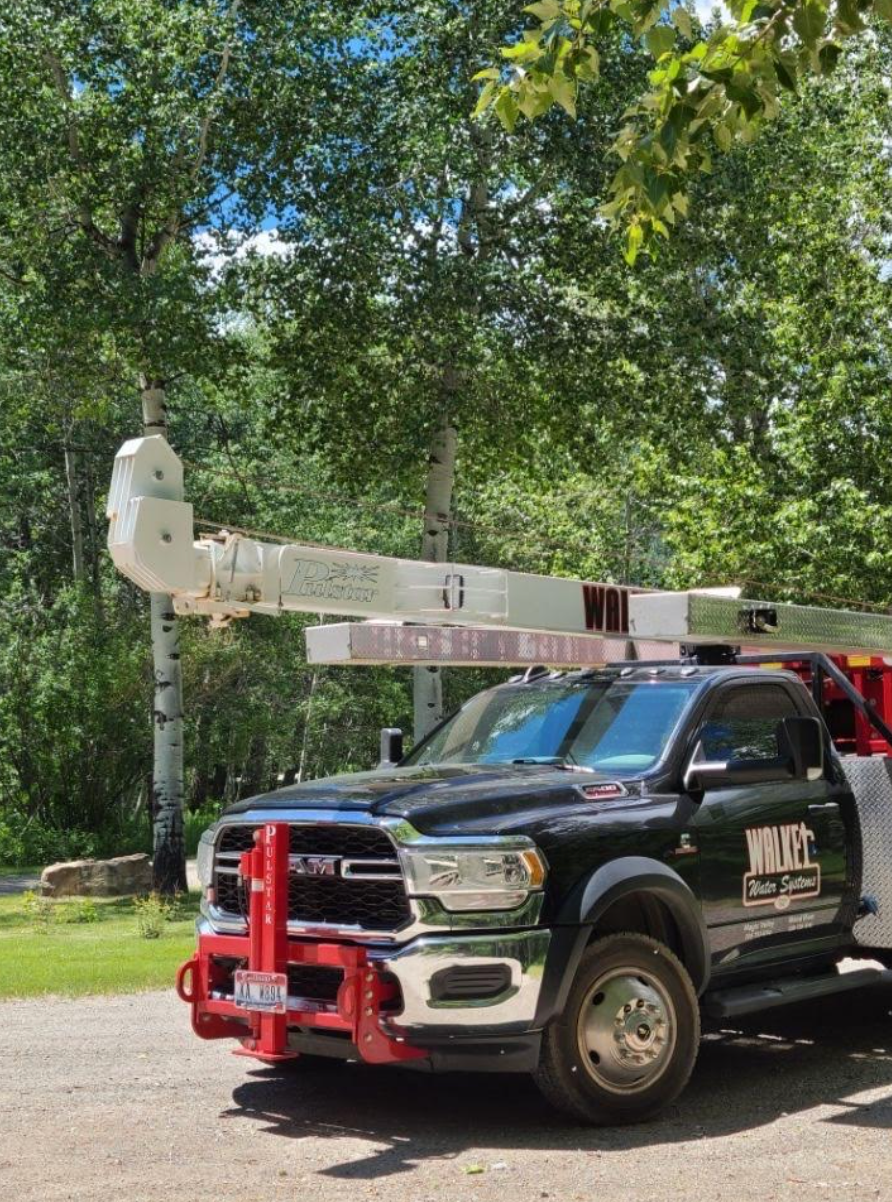 Black utility truck with raised boom parked outdoors under trees.