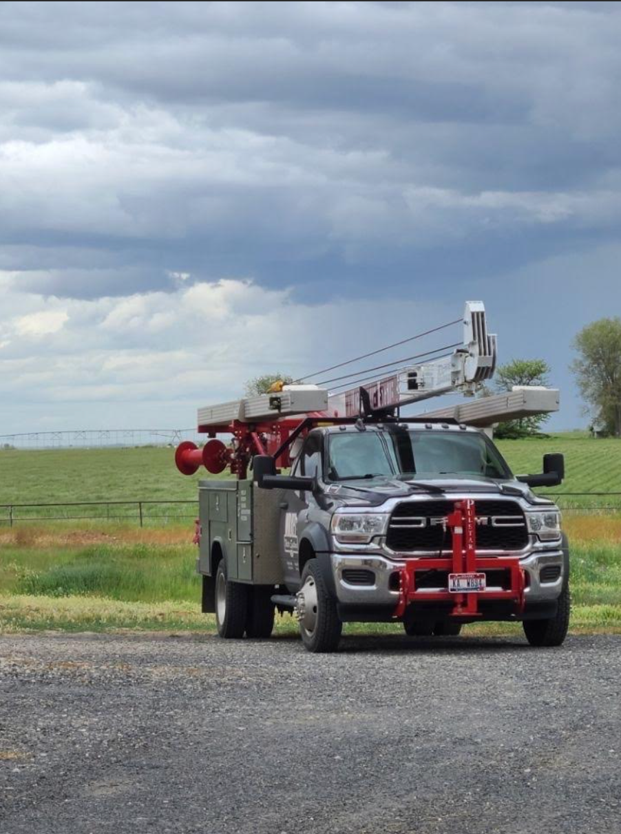 Red fire truck with extended ladder parked on a gravel road under cloudy skies in a grassy field