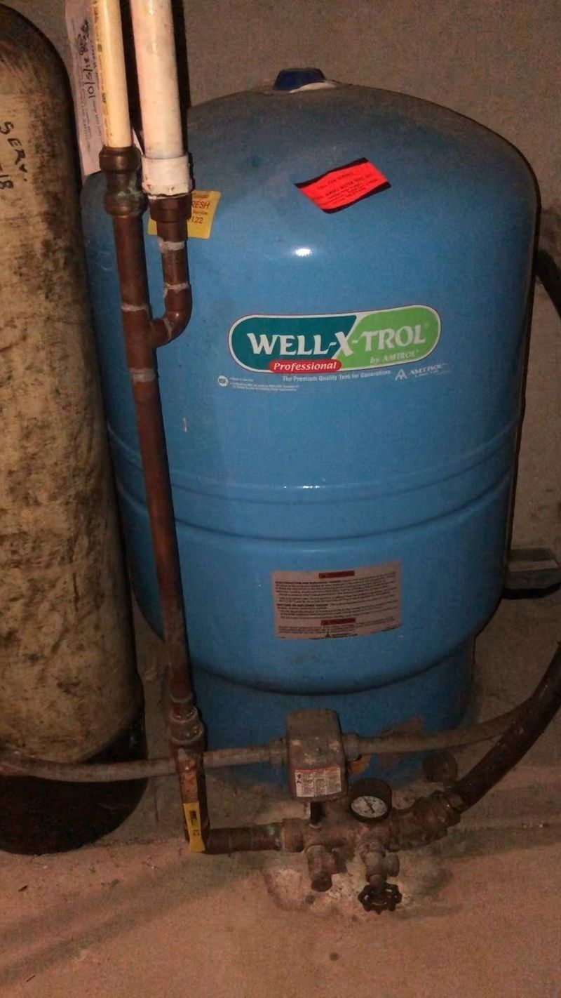 Blue Well-Trol water pressure tank with pipes and valve in a basement or utility room
