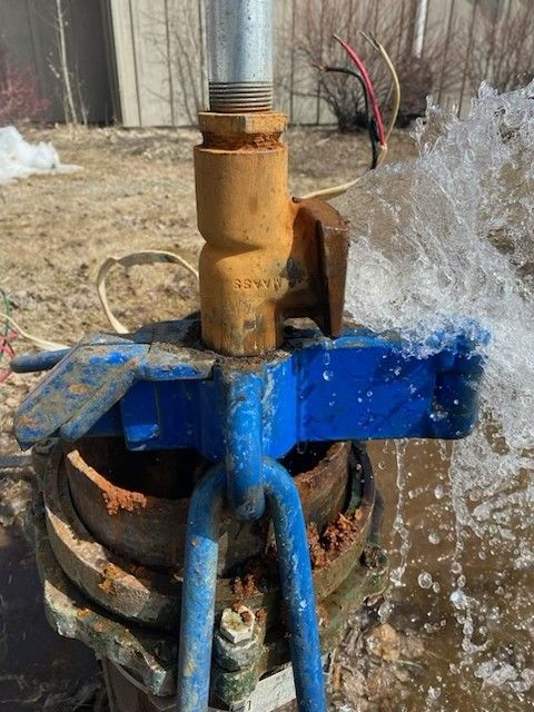 Blue irrigation valve spraying water outdoors, with a rusty pipe and splashing stream