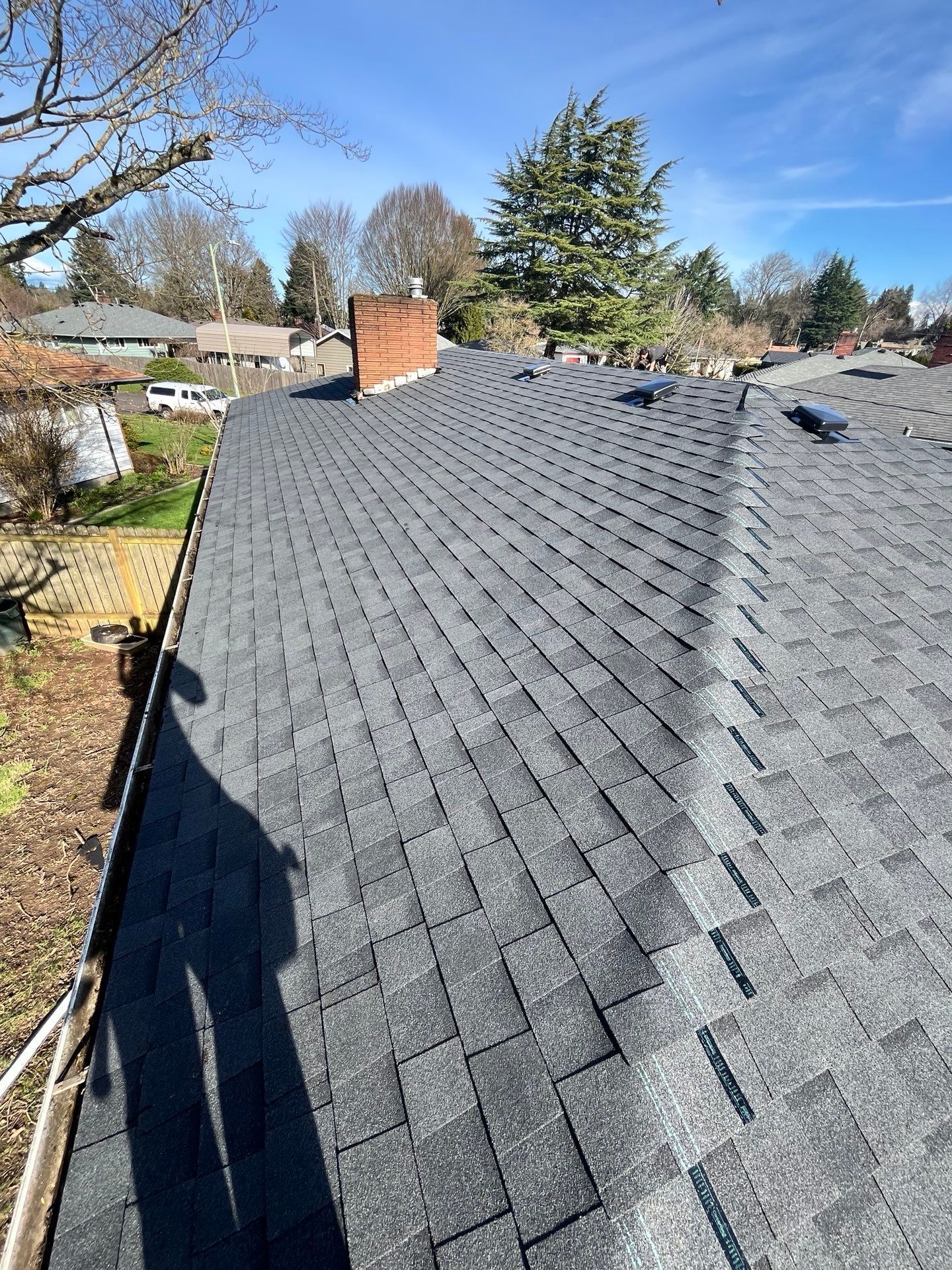 Dark gray asphalt shingle roof with a brick chimney under a blue sky.
