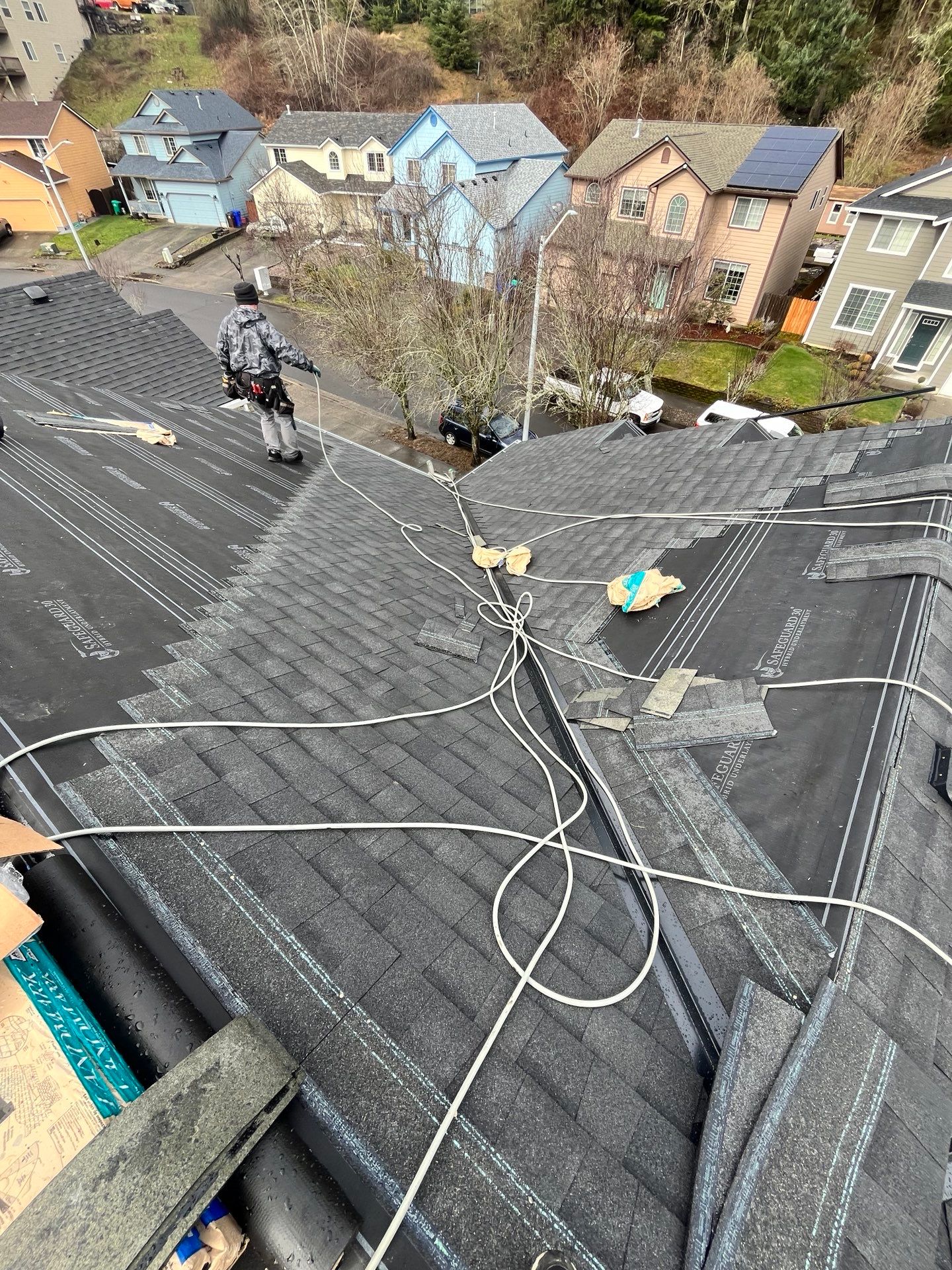 Roofer working on a residential rooftop with partial shingle removal, surrounded by neighborhood houses.