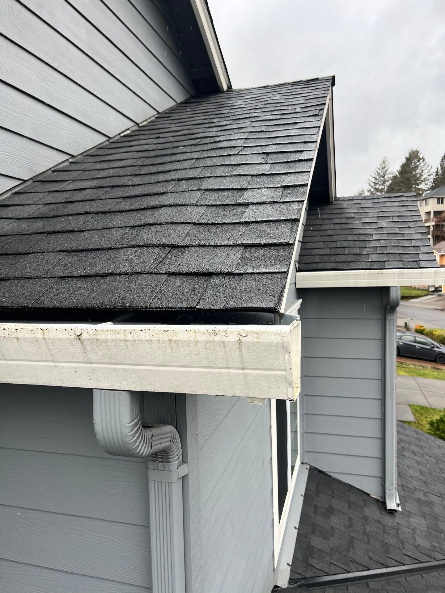 Gray house roof with dark shingles, white gutters, and blue siding.