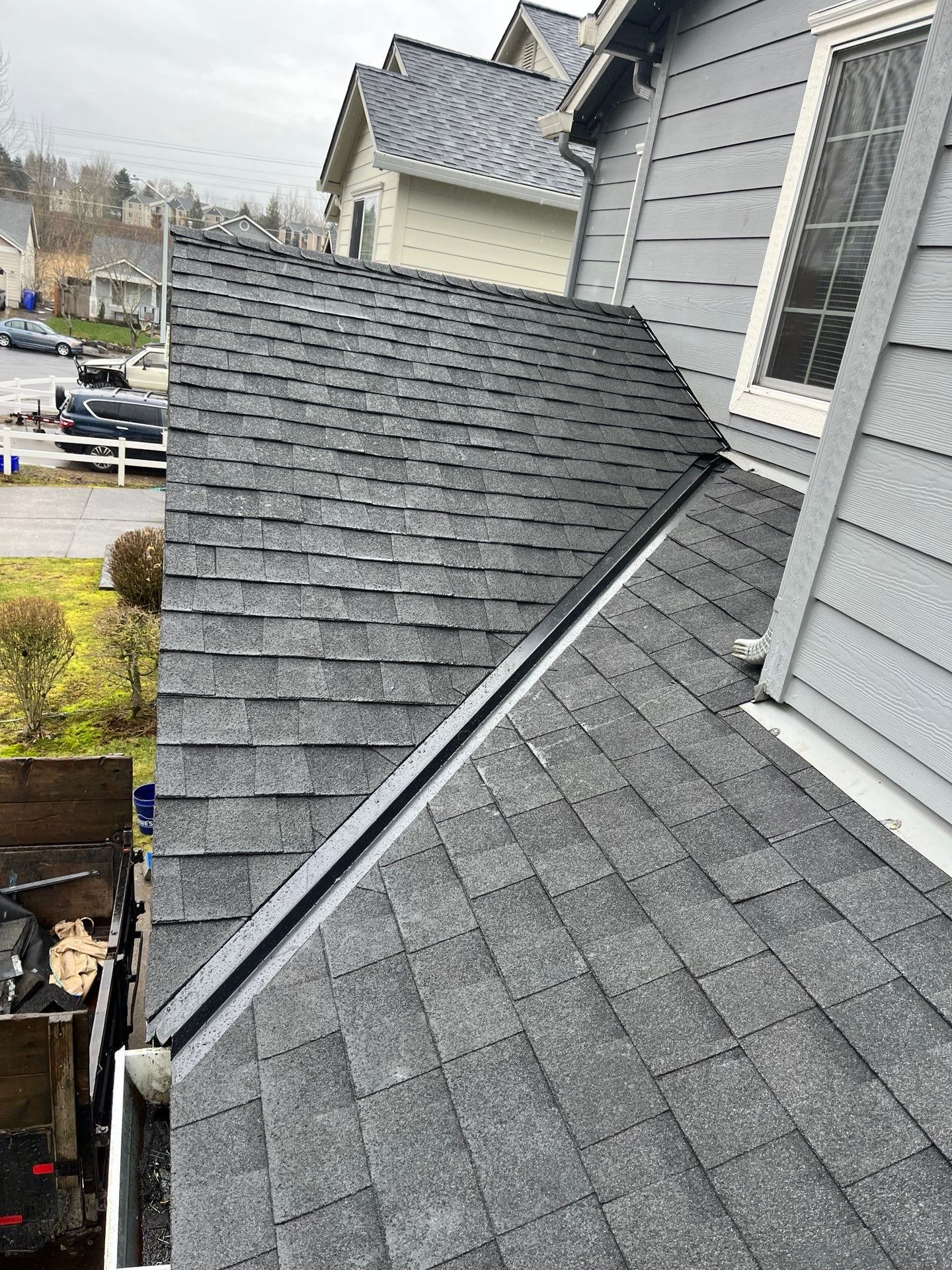 Gray asphalt shingle roof with black metal flashing and gutter, attached to a gray house, overcast outdoor setting.