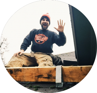Two roofers installing plywood on a roof. Tools and materials are scattered around the work area.