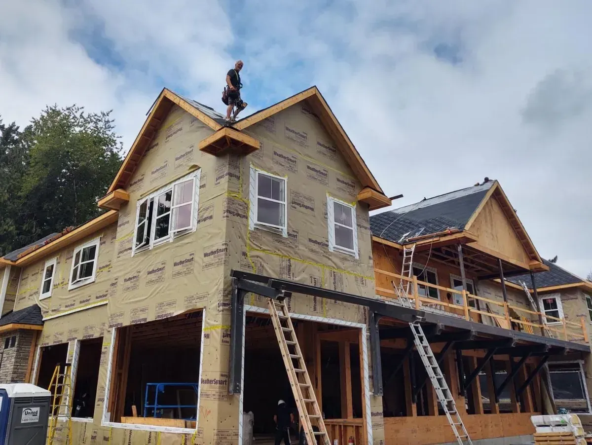 Construction worker on roof of a house. House is in progress, with visible framing and sheathing. Cloudy sky.