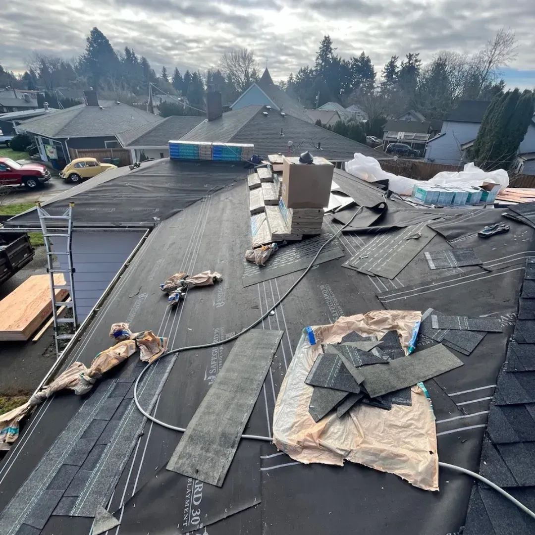 Roof under construction; black tar paper, shingles, and supplies on a house roof in a suburban setting.