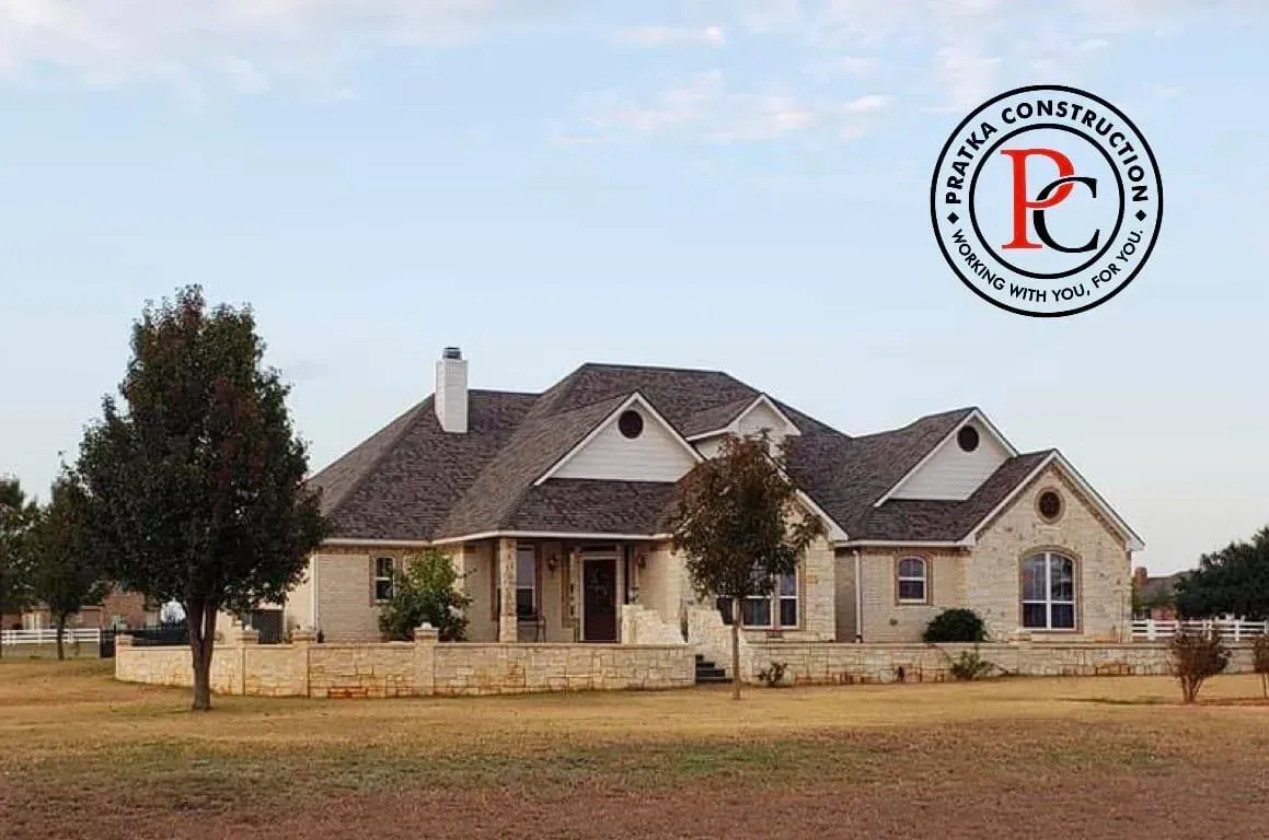 A ranch-style home with stone facade and a company logo in the sky, in a field.