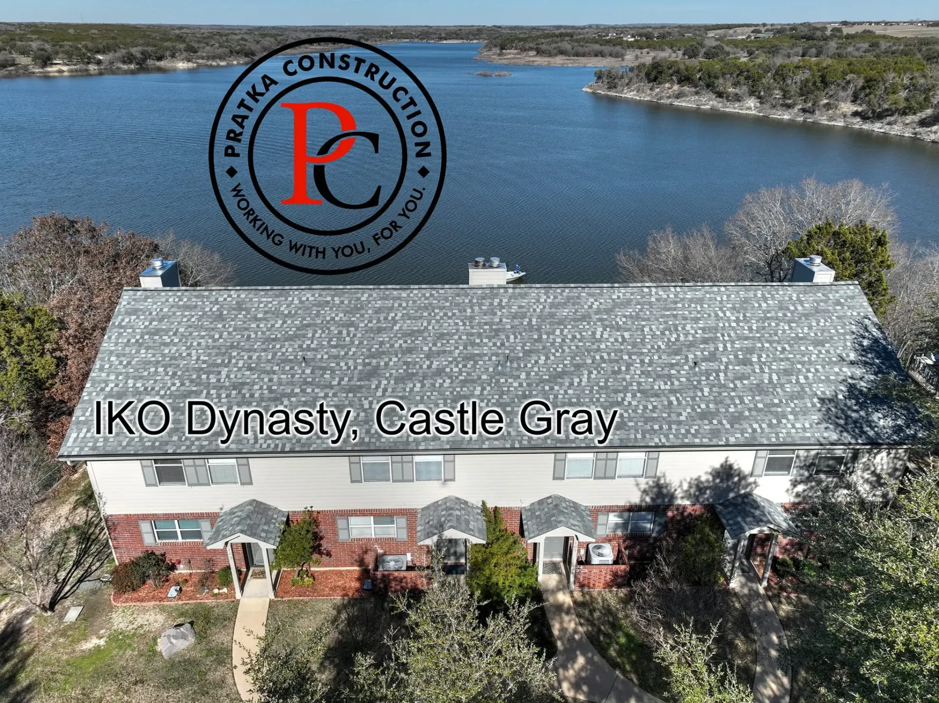 Row of homes with gray roofs on a lake, Praska Construction logo, text: IKO Dynasty, Castle Gray.