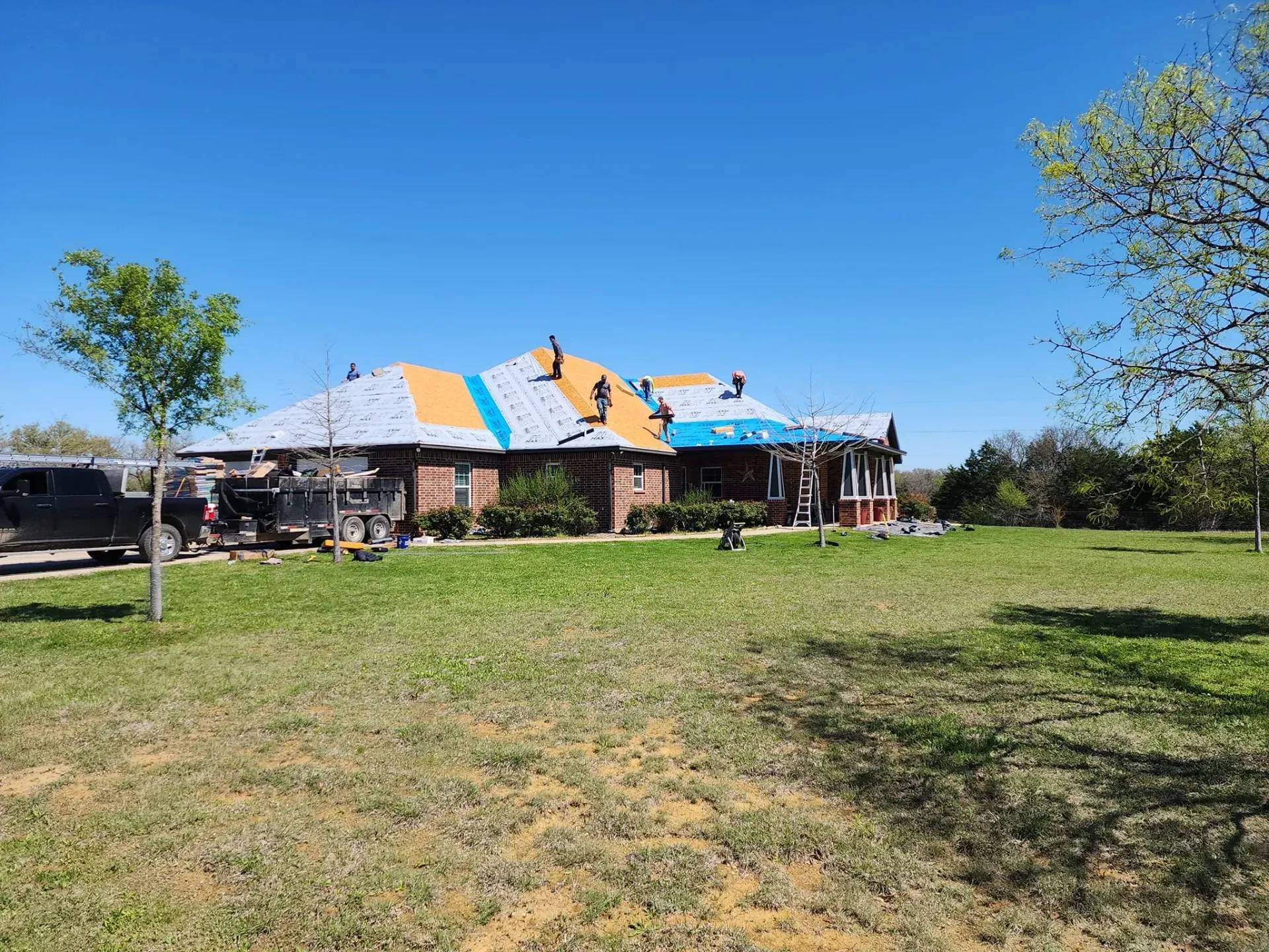 Roofers working on a brick house with a partly completed roof, on a sunny day.