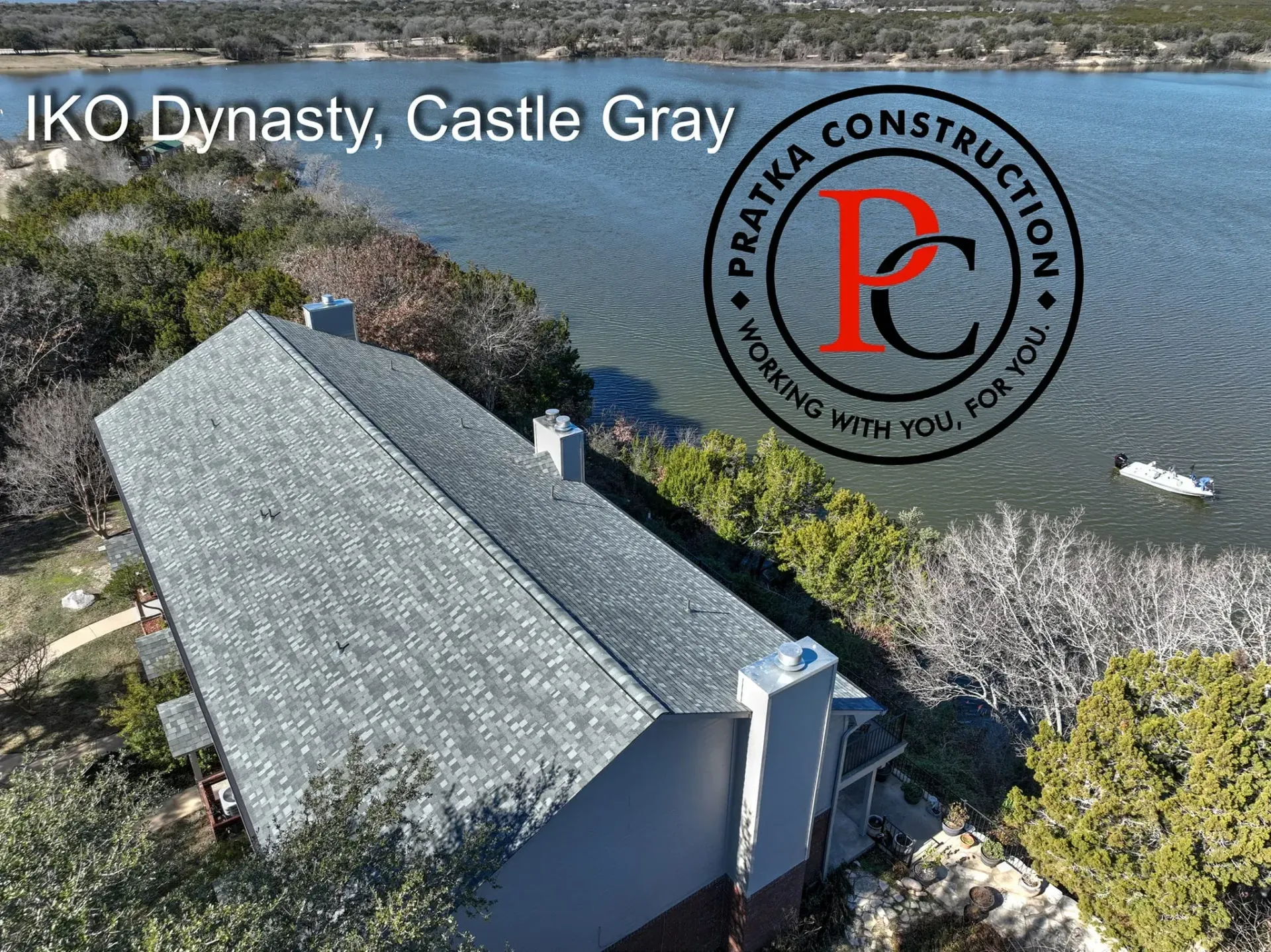 Aerial view of a house with a gray roof, IKO Dynasty Castle Gray, by a lake; Pratka Construction logo.