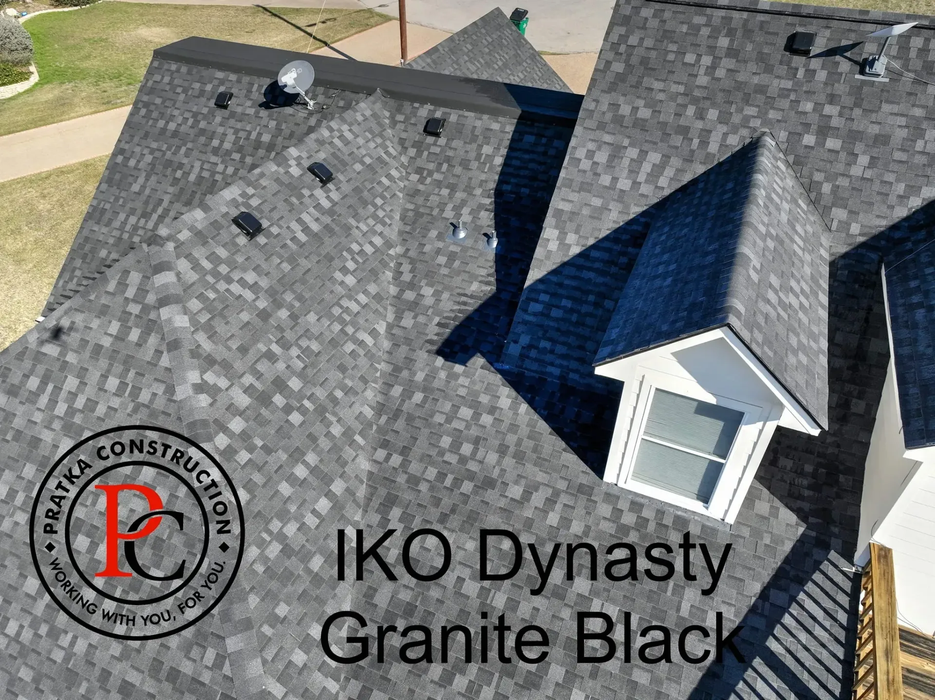 Overhead view of a house roof with black granite shingles and a dormer. Text: IKO Dynasty Granite Black.