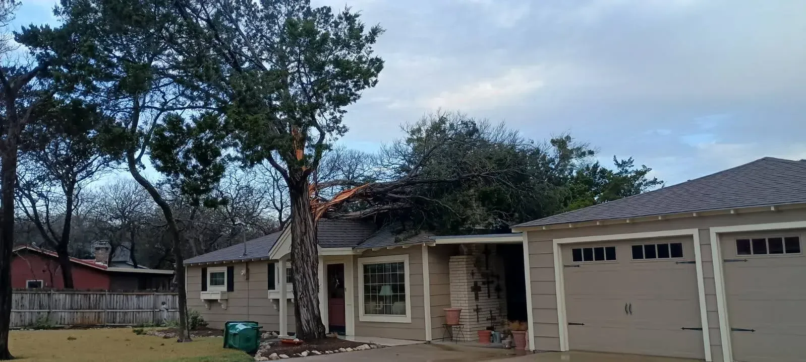 House with trees and a garage under a cloudy sky.