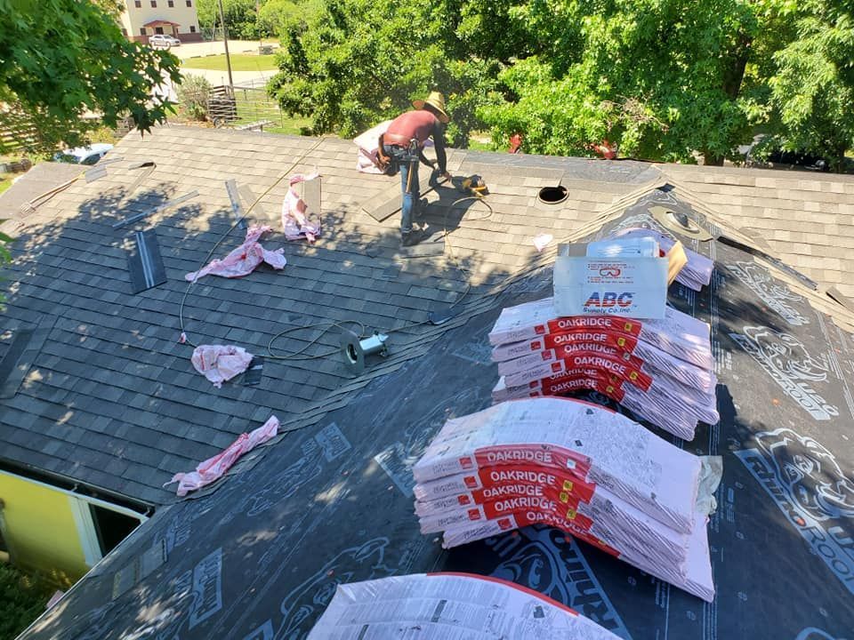 Workers on a roof installing insulation and shingles on a sunny day.